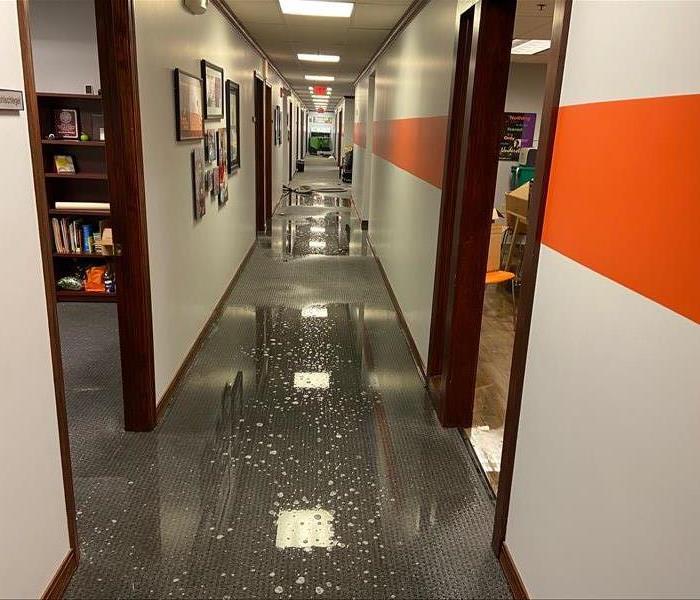 Hallway in business with water soaked floor, orange stripe down wall, drop ceiling and multiple doorways.