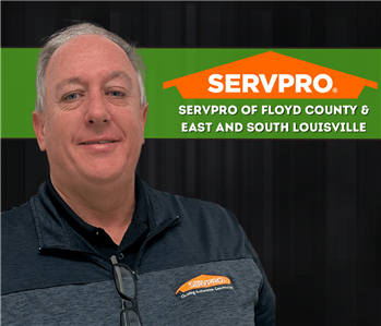 A man in a SERVPRO shirt smiling at the camera with a black  backdrop and a SERVPRO logo